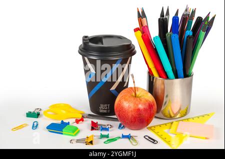 Una collezione di vivaci forniture per ufficio con una tazza di caffè, mela, graffette, fermagli leganti, perni a pressione, cancellatori. Foto Stock