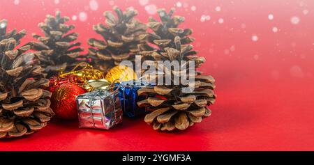 Disposizione a tema natalizio con coni di pino e piccoli regali avvolti su uno sfondo rosso brillante con fiocchi di neve cadenti. Foto Stock