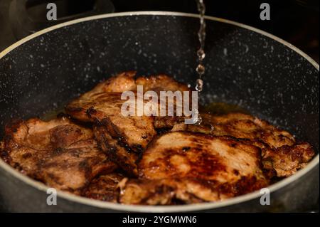 Le morbide costolette di maiale sfrigolano in una padella, con acqua che si spruzza mentre cucinano alla perfezione sul piano cottura. Foto Stock