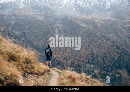 Solo escursionista che si affaccia su una vastissima valle autunnale da un aspro sentiero Foto Stock