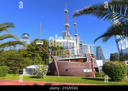 Batumi, Georgia, 30 aprile 2017: Parco con palme, nave e case moderne vicino al lungomare della località estiva georgiana, in Asia Foto Stock