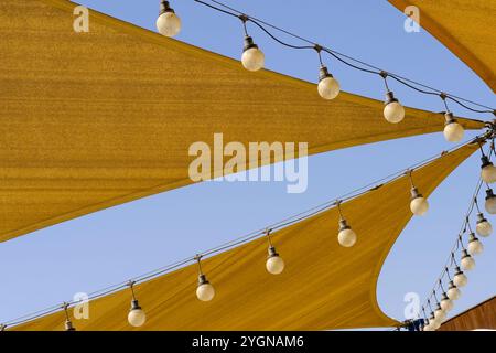 Telo da sole in tessuto con teglia a vela con file di lampade a sospensione su sfondo blu. Foto Stock