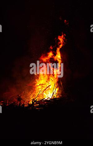 Grande falò con fiamme che sparano in aria di notte. Il fuoco ha i colori rosso, arancione e giallo. Ci sono scintille che volano in aria Foto Stock