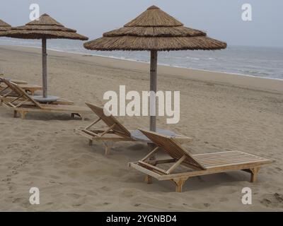 Diverse sdraio in legno sotto i tetti di paglia sono allineate lungo una spiaggia sabbiosa con vista mare, katwijk, mare del nord, paesi bassi Foto Stock