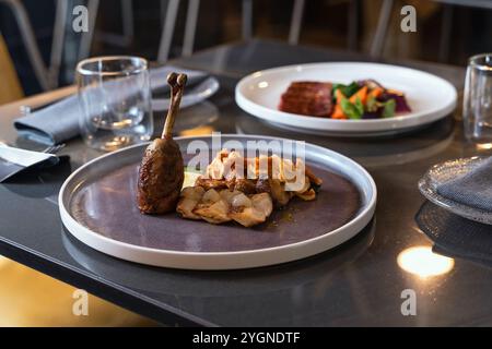 Gamba d'anatra confit con funghi arrostiti serviti su un piatto di ceramica moderno presso un raffinato ristorante, cena gourmet di presentazione Foto Stock