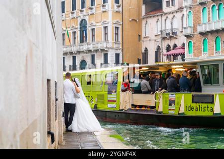 Coppia nuziale in posa accanto al canale di Venezia e il taxi boat è di passaggio Foto Stock