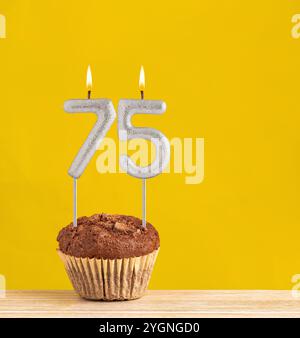 Candela di compleanno numero 75 - cupcake al cioccolato su sfondo giallo. Foto Stock