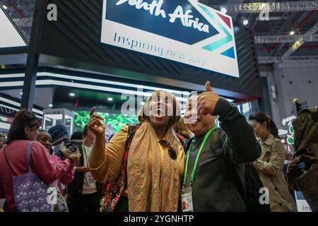 Shanghai. 8 novembre 2024. Un visitatore posa per le foto con un espositore al Padiglione Sud Africa durante la settima China International Import Expo (CIIE) nella zona orientale di Shanghai, 8 novembre 2024. L'attuale edizione del CIIE ha ulteriormente ampliato la scala espositiva per i paesi e i marchi africani nell'area Country Exhibition e nell'area Food and Agricultural Products, dove viene presentata una vasta gamma di prodotti africani di alta qualità con caratteristiche distintive. Crediti: Wang Yijie/Xinhua/Alamy Live News Foto Stock