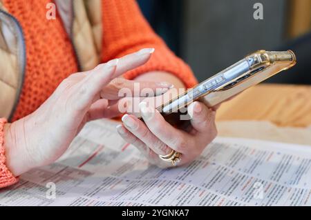 Mani che tengono lo smartphone sopra un documento cartaceo, che mostra il multitasking e la tecnologia moderna, ideali per progetti aziendali e di stile di vita. Foto Stock