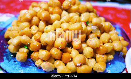 Primo piano di purcedduzzi o Struffoli, un tradizionale dolce natalizio italiano, ricoperto di sprinkles colorati, miele e servito su un piatto di vetro blu. Foto Stock