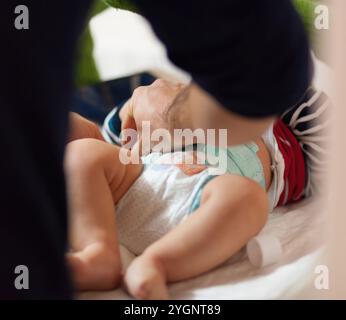 Padre che cambia il pannolino del suo bambino su un tappeto, mostrando amore e cura. Le mani assicurano delicatamente igiene e sicurezza, mettendo in risalto le gioie della genitorialità. Selettivo Foto Stock