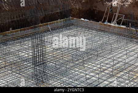 Barre di rinforzo in acciaio che formano una struttura a griglia per la fondazione di un edificio in un cantiere edile, preparazione per il versamento di calcestruzzo Foto Stock