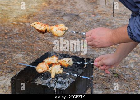 Uomo che frigge la carne alla griglia. Cuocere a fuoco le patatine fritte. Barbecue all'aperto. Bokeh brillante. Foto Stock