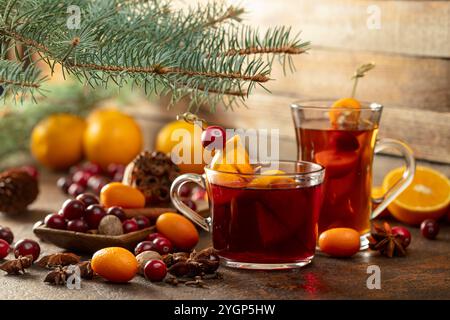 Bevande invernali con ingredienti su un vecchio tavolo da cucina. Sul tavolo sono sparsi mirtilli rossi, kumquat, arance, anice, cannella, noce moscata e chiodi di garofano. Foto Stock