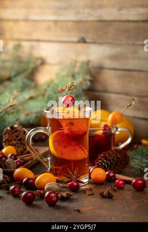 Bevande invernali con ingredienti su un vecchio tavolo da cucina. Sul tavolo sono sparsi mirtilli rossi, kumquat, arance, anice, cannella, noce moscata e chiodi di garofano. Foto Stock