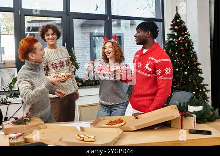 I colleghi festivi si godono la pizza e le risate mentre festeggiano il Natale nel loro allegro ufficio. Foto Stock