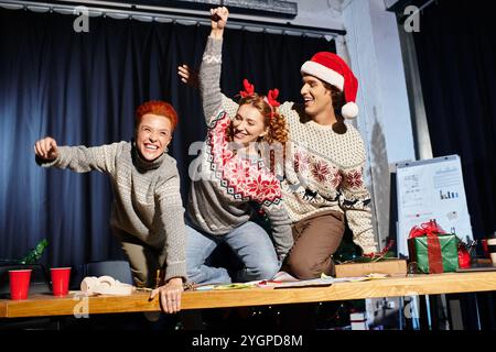 Tre colleghi esprimono gioia ed entusiasmo mentre celebrano il Natale nel loro ufficio. Foto Stock