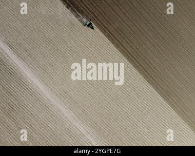 Vista aerea di un agricoltore che guida un trattore e ara un campo, preparandosi per il raccolto. Foto Stock