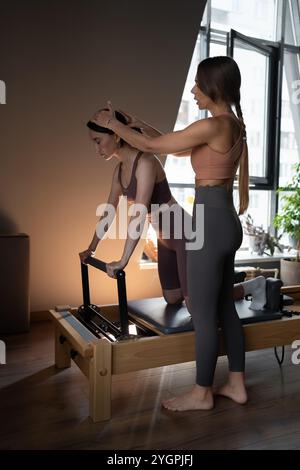 Donna che allena pilates sul letto del riformatore con l'addestratore. Riformatore pilates macchina da studio per allenarsi in palestra. In forma, sano e forte Foto Stock