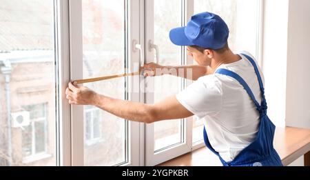 Lavoratore maschio con righello a nastro per l'installazione di finestre in piano Foto Stock