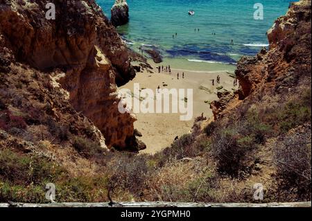 Insenatura isolata e soleggiata con amanti della spiaggia, annidata tra le torreggianti scogliere. Foto Stock