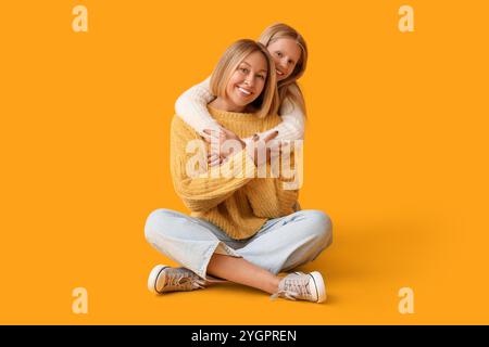 Bella donna e sua figlia in maglioni eleganti seduti su sfondo giallo Foto Stock