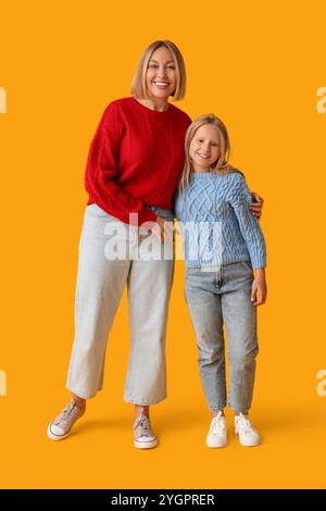 Donna felice e sua figlia carina in maglioni eleganti su sfondo giallo Foto Stock