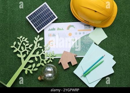 Pannello solare con figura della casa, albero di carta, lampadina e elmetto sull'erba. Concetto di energia verde Foto Stock