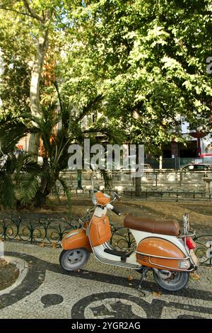 Lisbona, Portogallo - 18 agosto 2016: Vespa arancione d'epoca parcheggiata sotto un albero su una strada acciottolata. Foto Stock