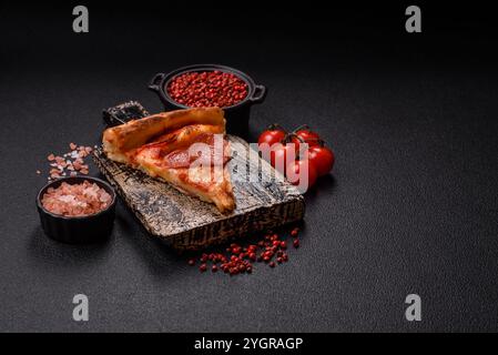 Pizza al peperoni con salsiccia, mozzarella, pomodori, sale e spezie su fondo di cemento scuro Foto Stock