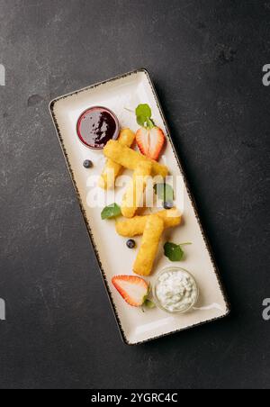 Bastoncini di formaggio croccanti serviti con salsa di frutti di bosco e salsa alle erbe su un piatto elegante, guarniti con frutta Foto Stock