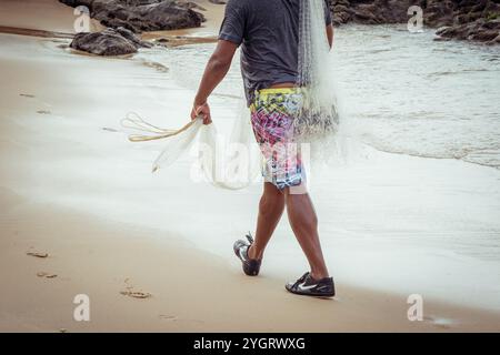 Salvador, Bahia, Brasile - 16 novembre 2019: Il pescatore è visto camminare sulla sabbia della spiaggia con reti da pesca e secchio. Città di Salvador, Bahia. Foto Stock