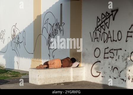 Un uomo dorme su una panchina di cemento in una chiesa accanto a un muro nella città di Salvador, Bahia. Foto Stock