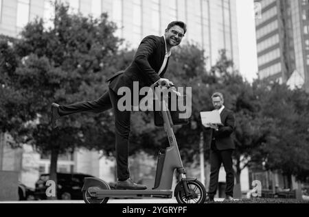 Business pazzo, veloce e facile. Uomo d'affari in tuta in sella a uno scooter elettrico in una riunione d'affari. Buon uomo d'affari con scooter all'aperto. Divertente Foto Stock