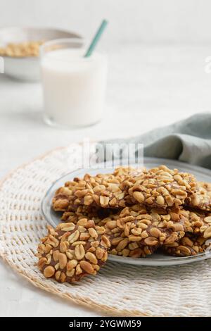 Un mucchio di tradizionali biscotti alle arachidi portoghesi conosciuti come Bolachas de Amendoim sul piatto grigio con un bicchiere di latte, un tovagliolo e un piatto di arachidi Foto Stock