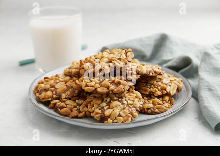 Un mucchio di tradizionali biscotti alle arachidi portoghesi conosciuti come Bolachas de Amendoim sul piatto grigio con un bicchiere di latte e tovagliolo su sfondo grigio Foto Stock