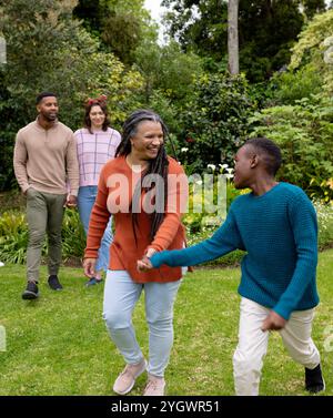 Periodo natalizio, famiglia multirazziale che si diverte a passeggiare all'aperto in giardino, sorridendo Foto Stock