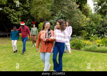 Periodo natalizio, famiglia multirazziale che si diverte a passeggiare in giardino, sorridendo Foto Stock