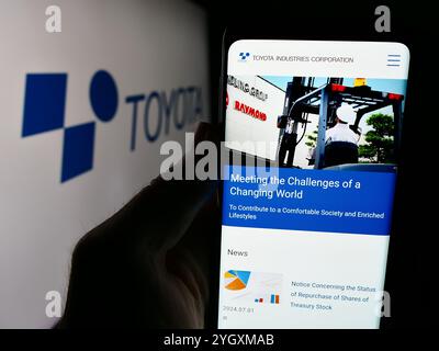 In questa illustrazione fotografica, una persona ha in mano uno smartphone con il sito Web dell'azienda giapponese Toyota Industries Corporation con il logo. Foto Stock