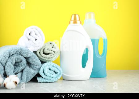 Detersivo per bucato in bottiglie, fiori di cotone e asciugamani su un tavolo in marmo grigio su sfondo giallo Foto Stock