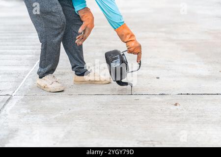 I lavoratori versano asfalto caldo sul pavimento in cemento per giunti in cantiere. Foto Stock