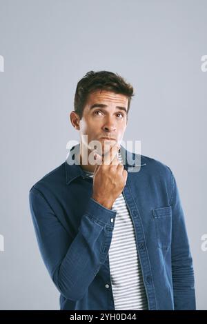 Uomo affascinante, pensiero e moda con decisione di scegliere, scegliere o cambiare outfit su uno sfondo da studio. Giovane, uomo o modello informale Foto Stock