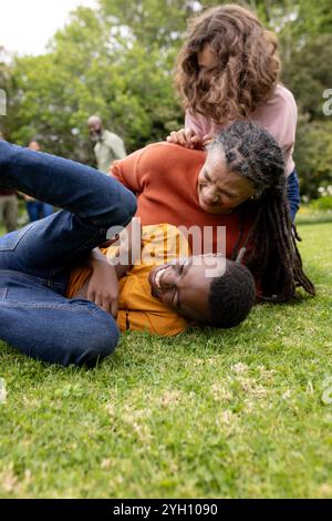 famiglia mutlirazziale che gioca sull'erba, ridendo e divertendosi all'aria aperta Foto Stock