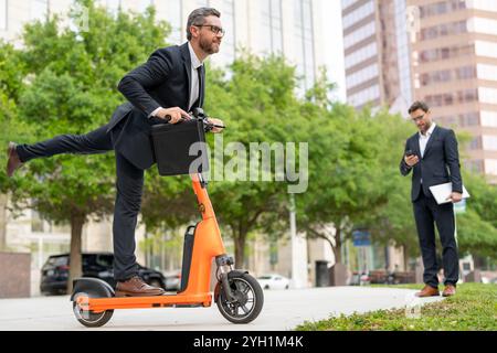 Un uomo d'affari entusiasta ha un aspetto cool e alla moda su uno scooter elettrico. Ecologico e veloce. Bell'uomo d'affari in scooter. Riunioni d'affari veloci Foto Stock