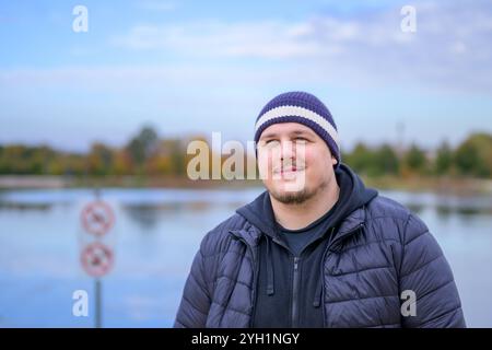 Un giovane uomo che indossa un berretto blu navy e bianco e una giacca nera a piumino sorride delicatamente mentre guarda in lontananza. Foto Stock