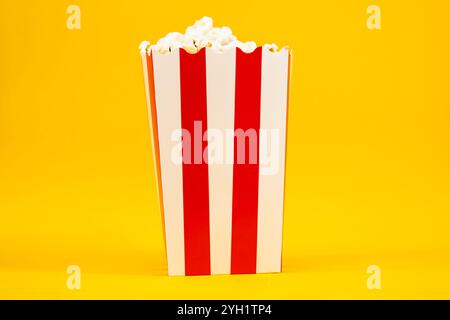 Popcorn in un secchio di cartone rosso e bianco su sfondo giallo, cinema e cibo Foto Stock