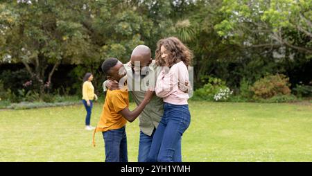 famiglia mutlirazziale che si diverte a abbracciare giocoso nel parco soleggiato, sorridendo e abbracciando insieme Foto Stock