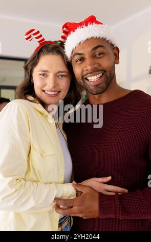 Coppia multirazziale sorridente che indossa cappelli festivi per festeggiare il Natale a casa insieme Foto Stock