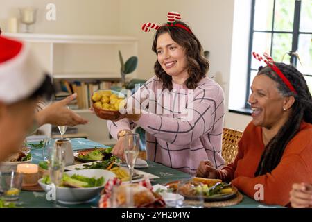 Famiglia multirazziale che condivide il pasto festivo, sorridendo e passando il cibo al tavolo di Natale, a casa Foto Stock