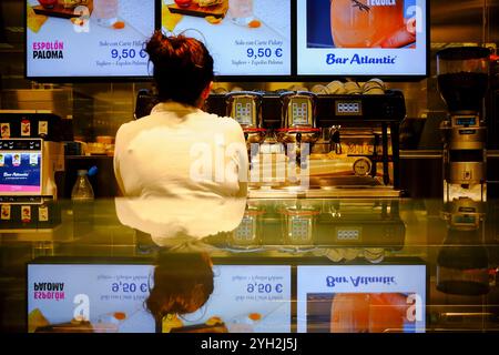 Traversetolo, Parma, Itally - 6 novembre 2024 Barista in piedi dietro il bancone con macchina per espresso e menu digitali con display cockt Foto Stock